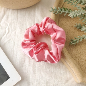 Detail of pink satin silk scrunchie showing glossy fabric texture and soft pleats