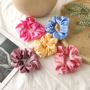 Detailed view of five colorful satin scrunchies arranged on a textured fabric backdrop