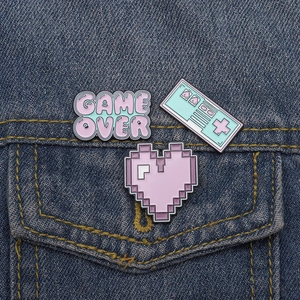 Three enamel gaming pins with Game Over text and heart on blue denim jacket pocket
