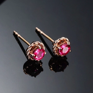 Detail of rose gold stud earrings with round faceted ruby and twisted rope border