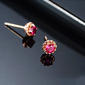 Close-up of rose gold rose flower earrings set with round red rubies on black surface