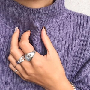 Close-up of stacked 925 sterling silver rings with white agate on purple knit sweater