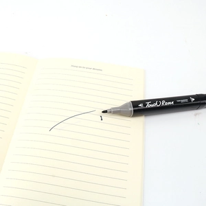 Detail of a black dual-tip permanent marker with broad and fine nibs on a notebook