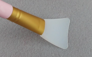 Close-up of silicone face mask brush with pink handle and flat white fan-shaped head