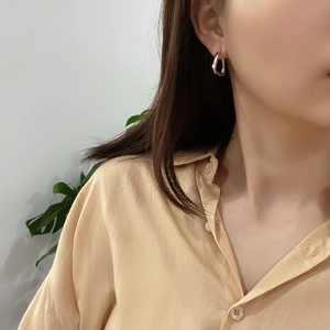 Close-up of minimalist silver geometric hoop earrings on model with mirror finish surface