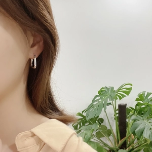 Close-up of minimalist silver geometric earring on model with monstera leaf background