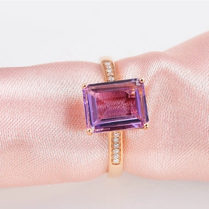 Macro shot of rectangular purple amethyst ring on pink silk fabric with rose gold plating
