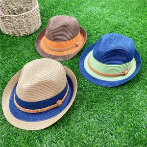Close-up of three woven straw fedoras in assorted colors on a lush green lawn