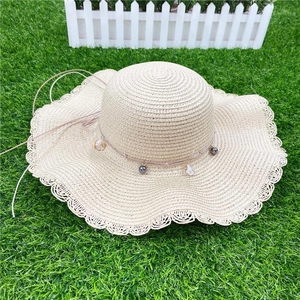Beige wide brim straw sun hat with gray beads and shell pendants on green grass