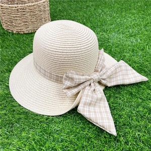 Wide brim straw sun hat with plaid ribbon bow on a green grass outdoor background