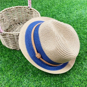 Women's straw fedora sun hat with dark blue ribbon on green grass for beach vacation