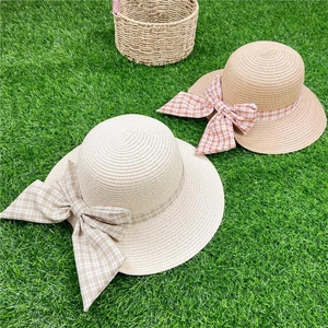 Flat lay of woven straw hats with plaid bows on green grass for beach vacation