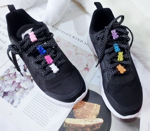 Detail of colorful gummy bear charms attached to black sneaker laces as bag decorations