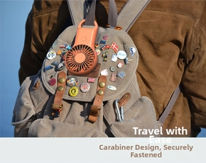 Orange portable mini fan with carabiner hanging on a backpack for outdoor travel