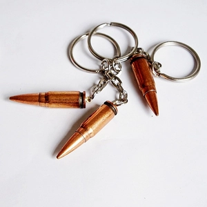 Close-up of three bronze bullet-shaped metal keychains with silver rings on white background