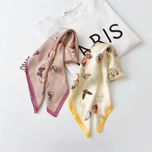 Close-up of square silk scarves in pink and beige with colorful butterfly patterns