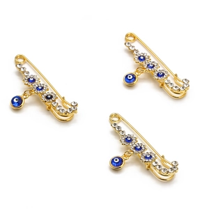 Golden angel wing brooches with evil eye pendants and blue gemstones on white background