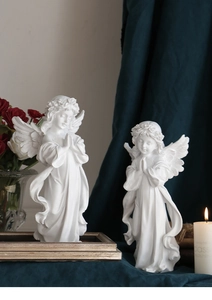 Detail of two white resin angel figurines on a vintage table with roses and candles