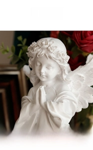 Close-up of a white resin angel sculpture with detailed wings and flower wreath decor