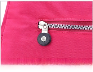 Detail of silver metal zipper with round puller on a rose red nylon crossbody bag