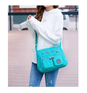 Detail of teal waterproof nylon crossbody bag showing multiple pockets on a model