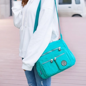 Detail of teal nylon multi-pocket crossbody bag shown worn in a lifestyle outdoor setting