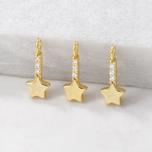 Detailed close-up of three gold star charms with zircon bars on marble background