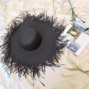 Black wide brim hand-woven straw hat with fringe edges on beige satin background