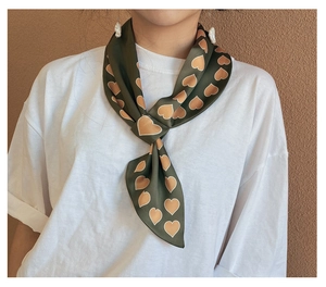 Dettaglio di un foulard di seta verde oliva con cuori arancioni annodato al collo