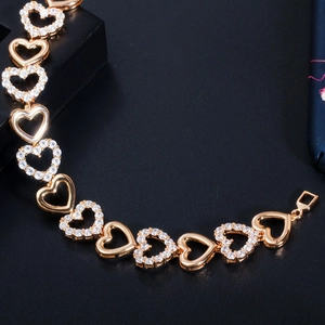Macro shot of gold heart-shaped bracelet links with sparkling inlaid zircons on dark background