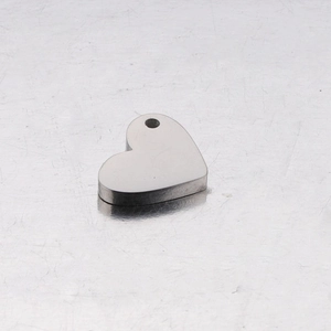 Polished heart-shaped stainless steel pendant with hole on a reflective metal surface