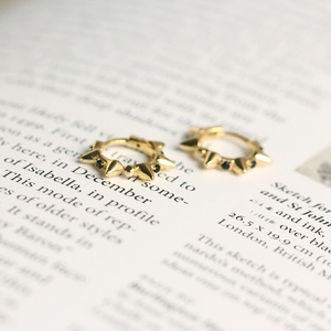 Detail of gold huggie earrings with pyramid studs and black gems on a book