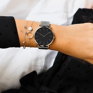 Detalle de reloj minimalista con esfera negra y correa de malla plateada con pulsera