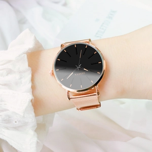 Primer plano de un reloj de oro rosa con correa de malla y esfera negra en la muñeca