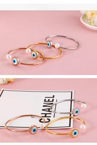 Detailed view of evil eye and pearl open bangles in gold, silver, and rose gold tones