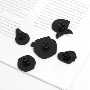 Detail view of five black enamel pin backs with butterfly clutches on book pages