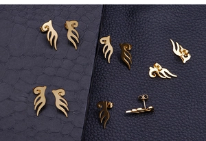 Detailed close-up of golden winged stud earrings on textured black leather backgrounds