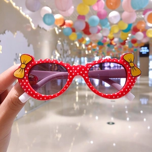 Detail view of red polka dot kids sunglasses with a yellow bow decoration and plastic frame