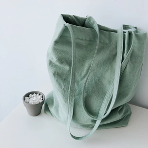 Detail of sage green washed cotton linen tote bag with natural fabric texture on white