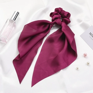 Detail of burgundy satin silk scrunchie with long ribbon on elegant white fabric