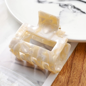 Macro detail of cream marble acetate hair claw clip showing glossy texture and hollow design