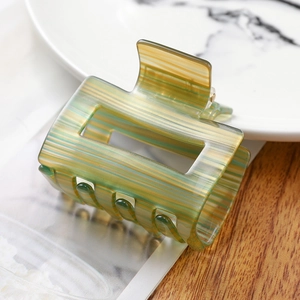 Detailed close-up of striped green and yellow acetate hair claw on a marble tray