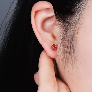 Close-up of rose gold flower stud earrings with red gemstone on model ear