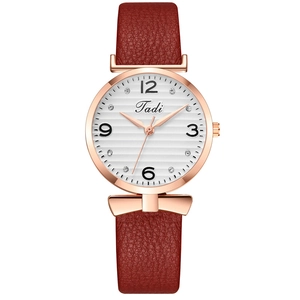 Détail du cadran en or rose avec index en strass et bracelet en cuir rouge avec nœud