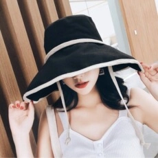 Dettaglio cappello da sole a tesa larga in contrasto bianco e nero con laccetto antivento