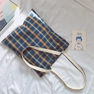 Close-up of blue and orange plaid canvas tote bag with thick woven straps on white fabric