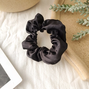 Close-up of black satin scrunchie with silky luster on a textured minimalist background