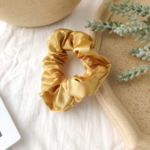Detailed view of champagne gold satin scrunchie on a stone tray with natural silk texture