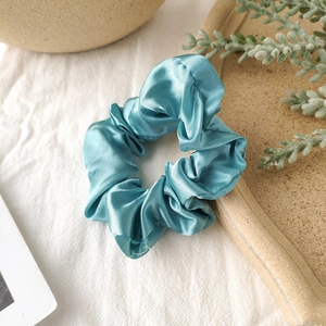 Close-up of light blue satin scrunchie on a ceramic tray with a soft silk texture