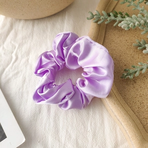 Detail of premium purple satin scrunchie showing glossy pleated texture and soft silk finish